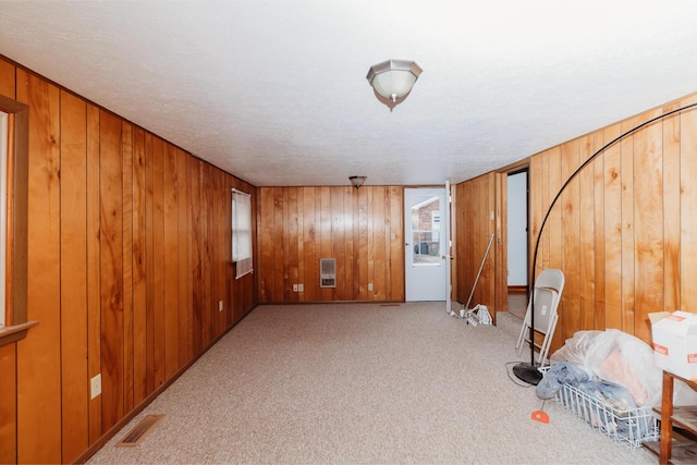 carpeted spare room with heating unit, wooden walls, and a textured ceiling