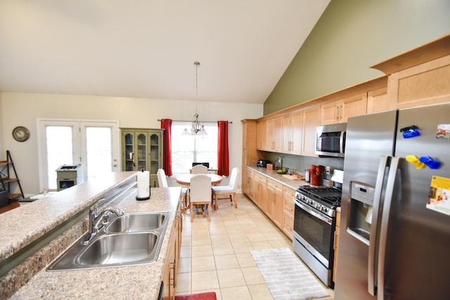 kitchen with appliances with stainless steel finishes, lofted ceiling, light brown cabinets, sink, and hanging light fixtures