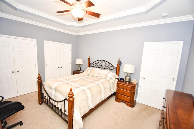 bedroom featuring light carpet, two closets, ceiling fan, a tray ceiling, and ornamental molding