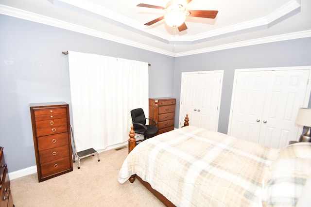 carpeted bedroom with ceiling fan, a tray ceiling, ornamental molding, and multiple closets