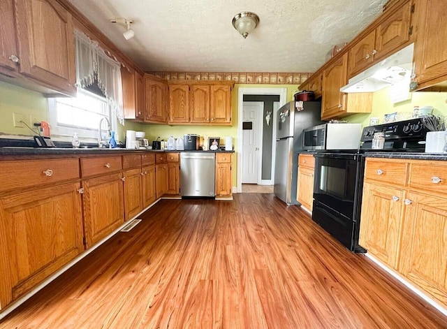 kitchen with sink, a textured ceiling, stainless steel appliances, and light wood-type flooring