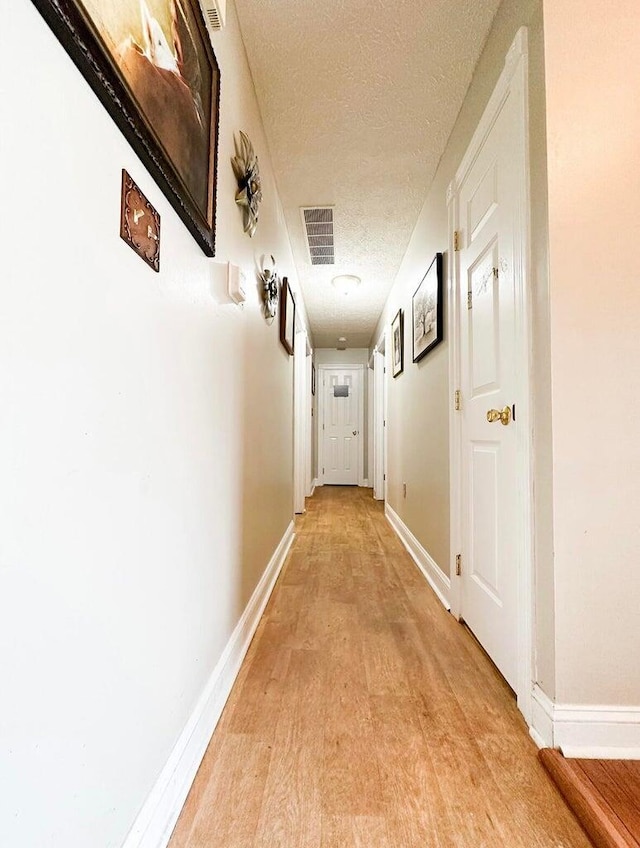 hall featuring a textured ceiling and light hardwood / wood-style floors