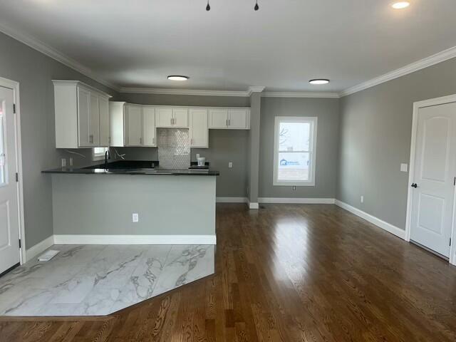 kitchen featuring kitchen peninsula, ornamental molding, decorative backsplash, and white cabinets