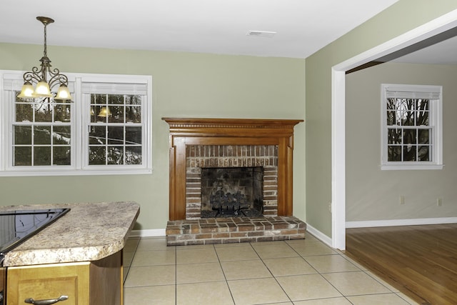 unfurnished living room with a brick fireplace, light tile patterned floors, and a notable chandelier