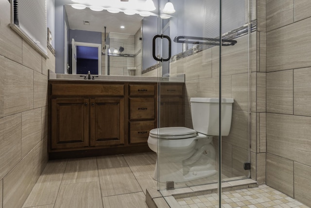 bathroom featuring toilet, vanity, tile walls, and a shower with door