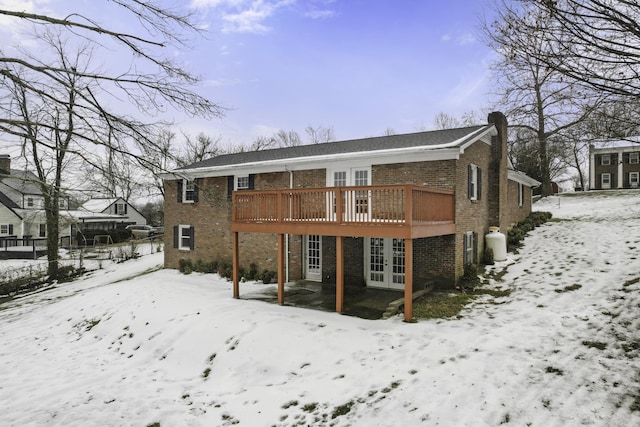 snow covered rear of property featuring french doors and a wooden deck