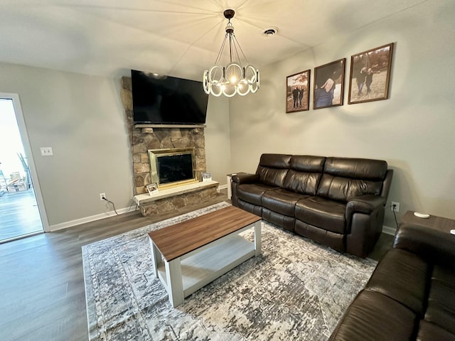 living room with wood-type flooring, a stone fireplace, and an inviting chandelier