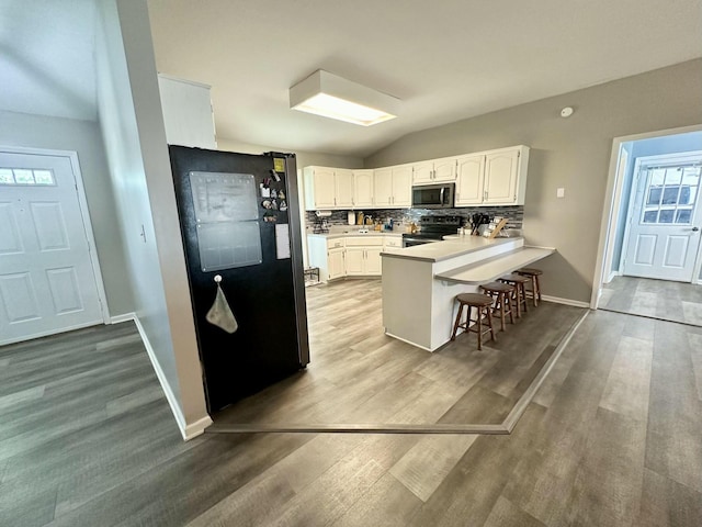 kitchen featuring white cabinets, stainless steel appliances, backsplash, kitchen peninsula, and a breakfast bar