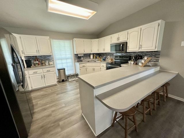 kitchen with kitchen peninsula, vaulted ceiling, stainless steel appliances, and white cabinetry