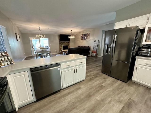 kitchen with a stone fireplace, stainless steel refrigerator with ice dispenser, hanging light fixtures, white cabinets, and dishwashing machine