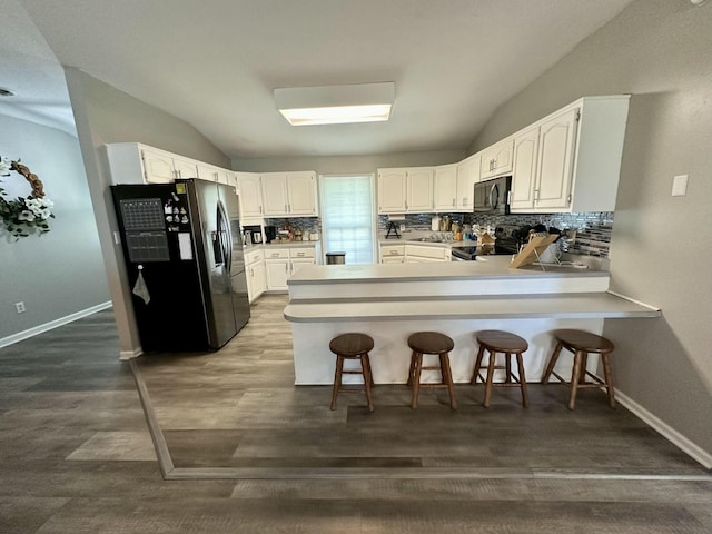 kitchen featuring kitchen peninsula, stainless steel refrigerator with ice dispenser, electric range oven, white cabinets, and a breakfast bar