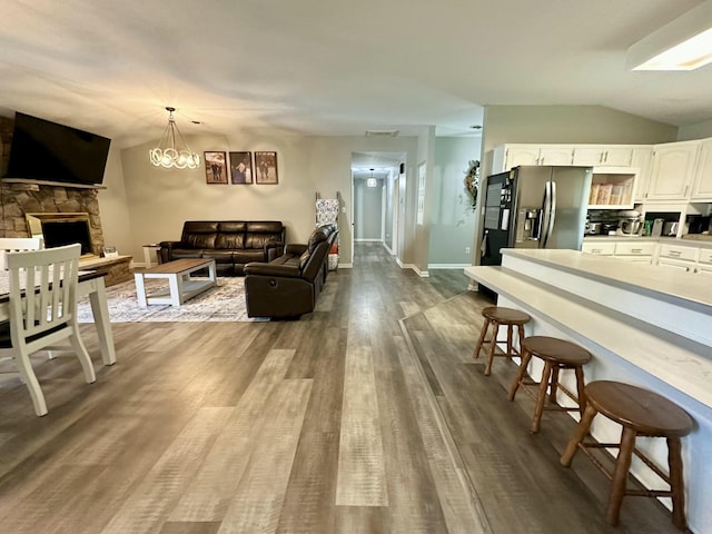 kitchen featuring white cabinetry, a kitchen bar, stainless steel refrigerator with ice dispenser, lofted ceiling, and hanging light fixtures