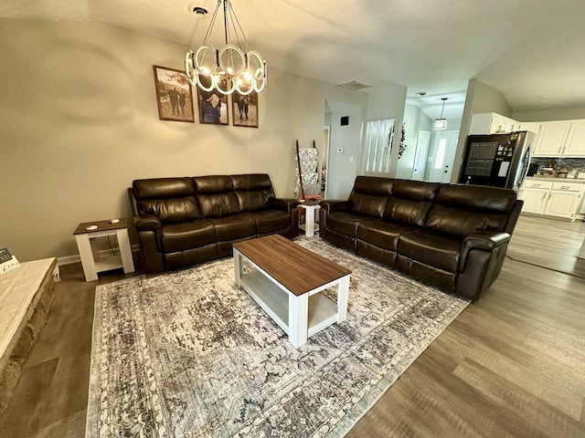 living room with vaulted ceiling, an inviting chandelier, and hardwood / wood-style floors