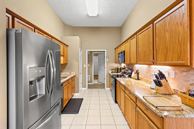 kitchen featuring decorative backsplash, light tile patterned floors, stainless steel appliances, light stone countertops, and a textured ceiling