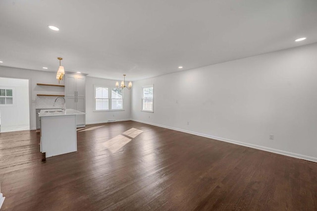 unfurnished living room with dark wood-type flooring, sink, and a chandelier