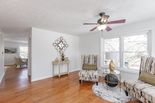 sitting room with ceiling fan, a textured ceiling, and light wood-type flooring