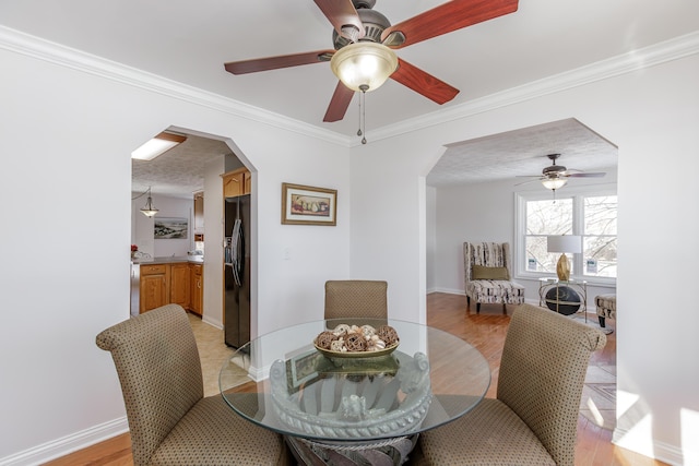 dining area featuring ceiling fan, a textured ceiling, ornamental molding, and light wood-type flooring