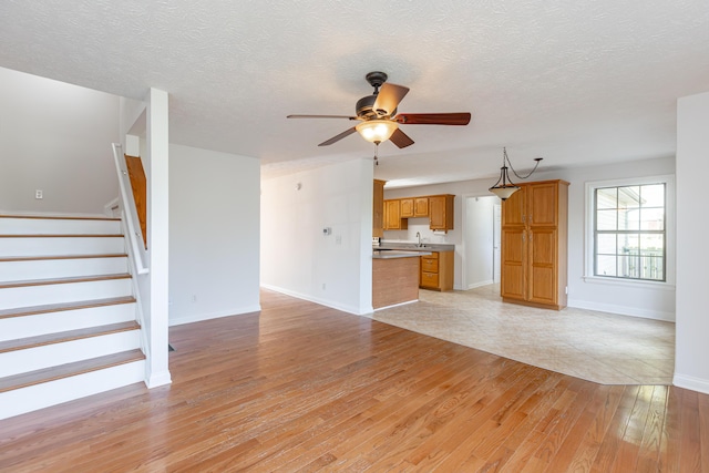 unfurnished living room featuring a textured ceiling, ceiling fan, light hardwood / wood-style floors, and sink