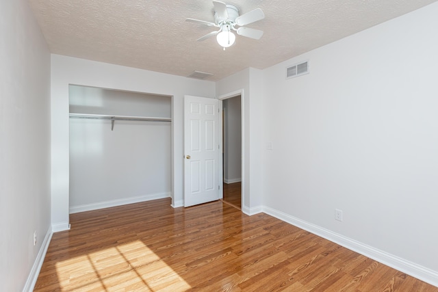 unfurnished bedroom featuring ceiling fan, a closet, a textured ceiling, and hardwood / wood-style flooring