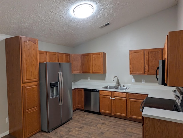 kitchen with appliances with stainless steel finishes, wood-type flooring, lofted ceiling, sink, and a textured ceiling