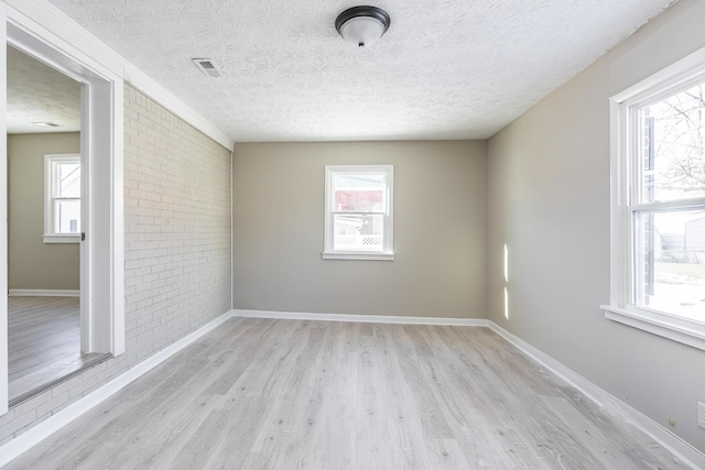 spare room with brick wall, light hardwood / wood-style flooring, and a textured ceiling