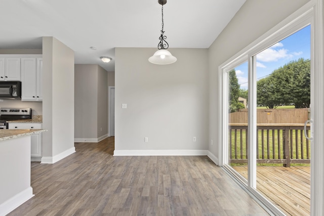 kitchen featuring electric stove, hardwood / wood-style flooring, hanging light fixtures, white cabinets, and light stone counters