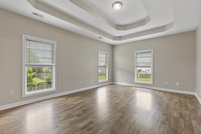 unfurnished room with dark wood-type flooring, plenty of natural light, and a tray ceiling