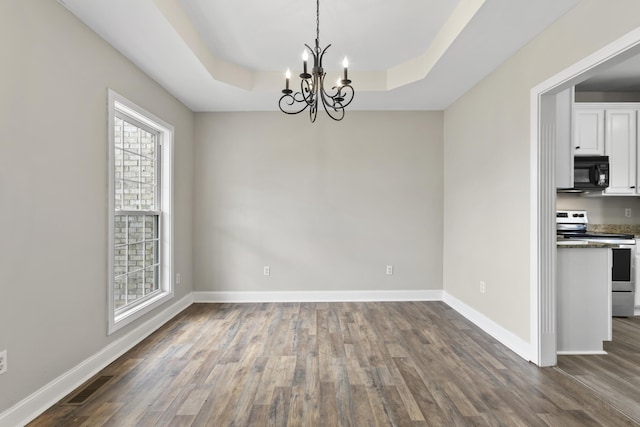 unfurnished dining area featuring an inviting chandelier, a tray ceiling, and dark hardwood / wood-style floors