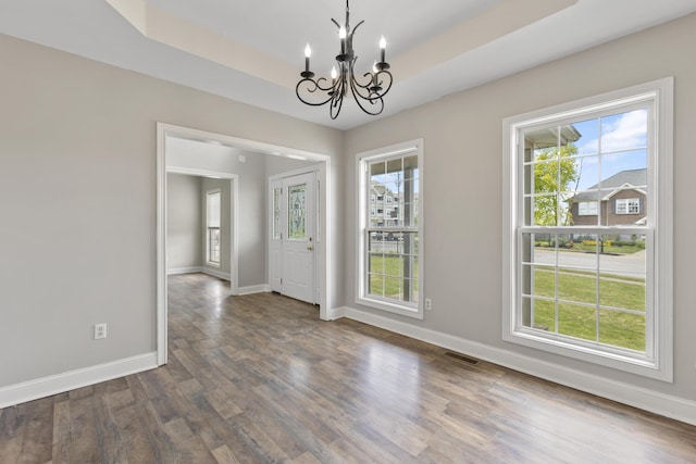 unfurnished dining area featuring plenty of natural light, dark hardwood / wood-style floors, a raised ceiling, and an inviting chandelier