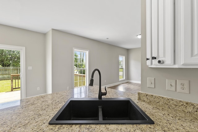 kitchen with light stone countertops, white cabinetry, and sink