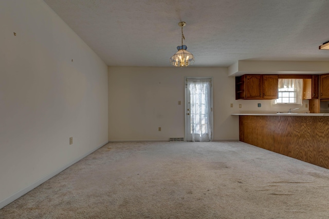 kitchen featuring kitchen peninsula, an inviting chandelier, hanging light fixtures, a textured ceiling, and light carpet