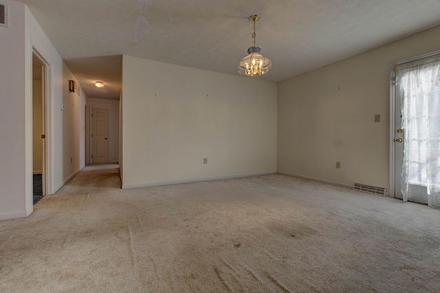 carpeted empty room with an inviting chandelier