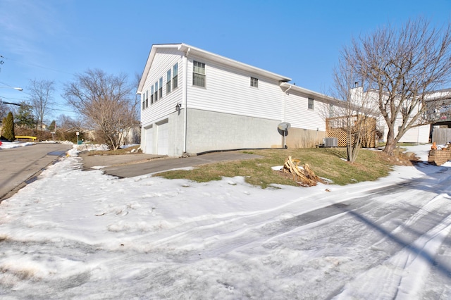 view of snowy exterior featuring central AC unit and a garage