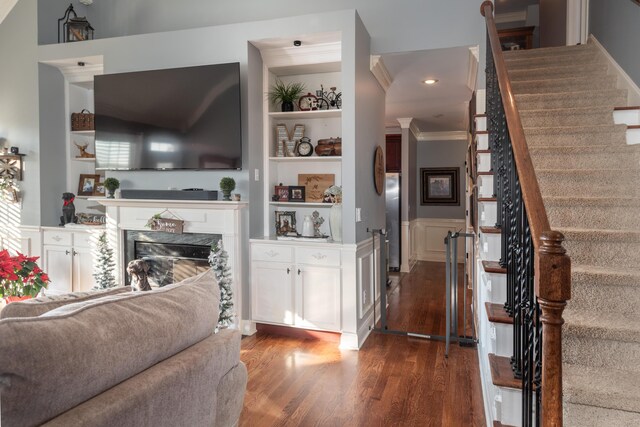 living room featuring dark wood-type flooring, a fireplace, ornamental molding, and built in features