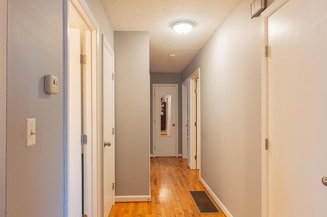 hallway with a textured ceiling and light hardwood / wood-style floors