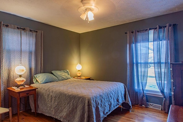 bedroom with a textured ceiling, a ceiling fan, and wood finished floors