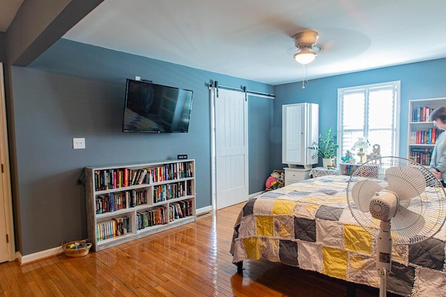 bedroom with hardwood / wood-style flooring, ceiling fan, and a barn door