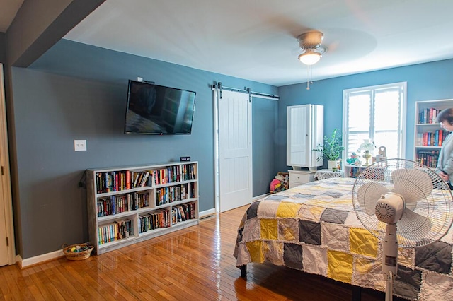 bedroom with a barn door, baseboards, hardwood / wood-style floors, and a ceiling fan
