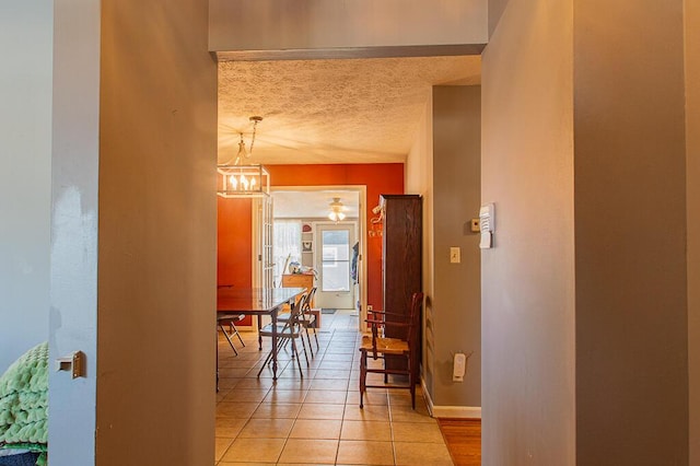 corridor featuring an inviting chandelier, baseboards, a textured ceiling, and light tile patterned flooring