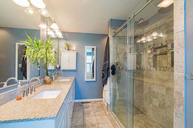 bathroom featuring a shower stall, double vanity, a sink, and baseboards