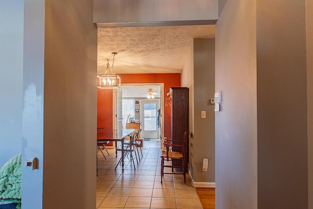 corridor featuring a chandelier, a textured ceiling, baseboards, and light tile patterned flooring