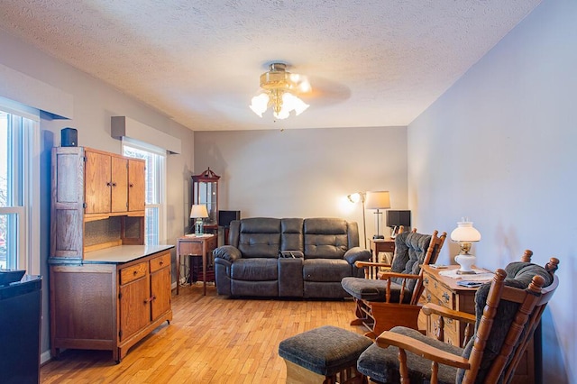 living room featuring light wood-type flooring, a ceiling fan, and a textured ceiling
