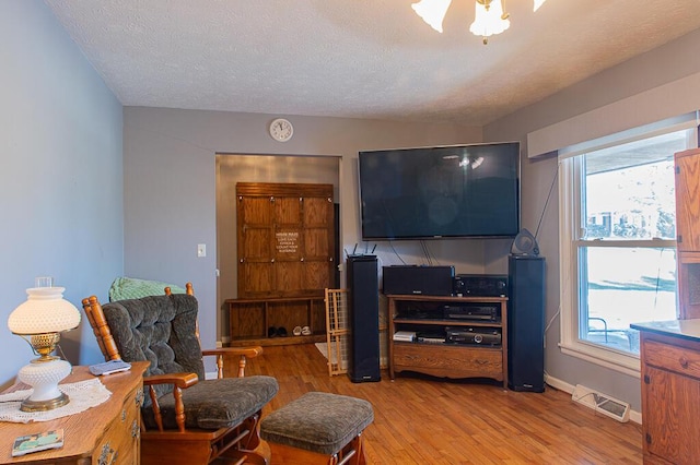 living room featuring visible vents, light wood-type flooring, a textured ceiling, and a healthy amount of sunlight