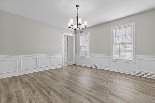 unfurnished room with a textured ceiling, a chandelier, and light hardwood / wood-style flooring