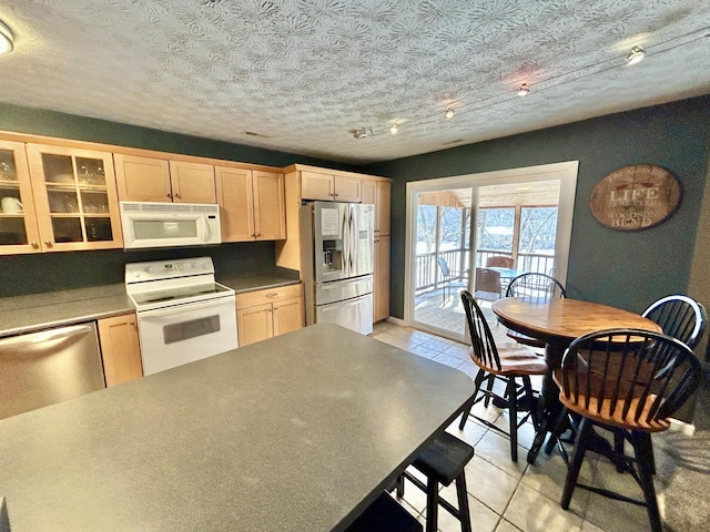 kitchen with light brown cabinetry, appliances with stainless steel finishes, light tile patterned flooring, and a textured ceiling