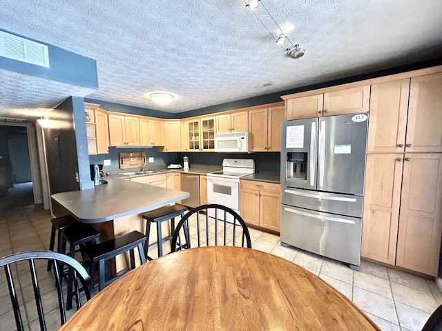 kitchen with light tile patterned floors, light brown cabinetry, appliances with stainless steel finishes, and a textured ceiling