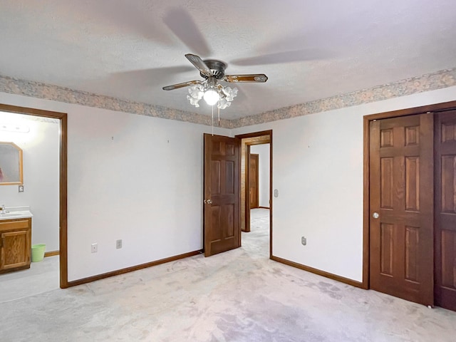 unfurnished bedroom featuring light carpet, a textured ceiling, ensuite bath, and ceiling fan