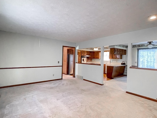 unfurnished living room with ceiling fan, a textured ceiling, and light carpet