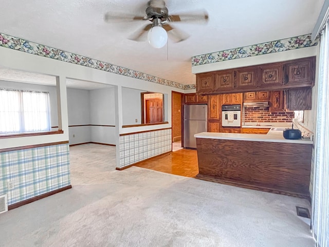 kitchen with stainless steel refrigerator, kitchen peninsula, white oven, ceiling fan, and light parquet flooring