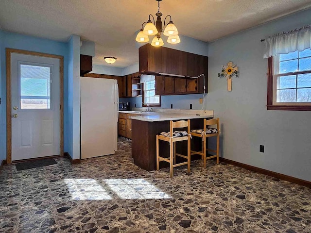 kitchen with kitchen peninsula, sink, white refrigerator, decorative light fixtures, and a kitchen bar